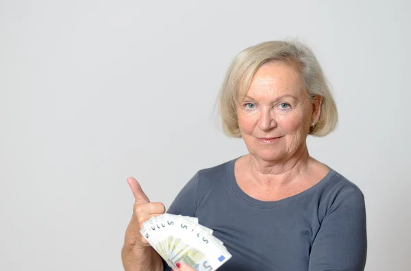 Старшая женщина держит вентилятор евро с поднятыми пальцами — стоковое фото