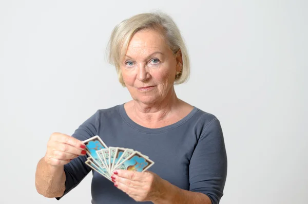 Старшая женщина держит карты Таро против серой стены — стоковое фото