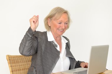Senior woman in business look in front of a silver laptop clipart