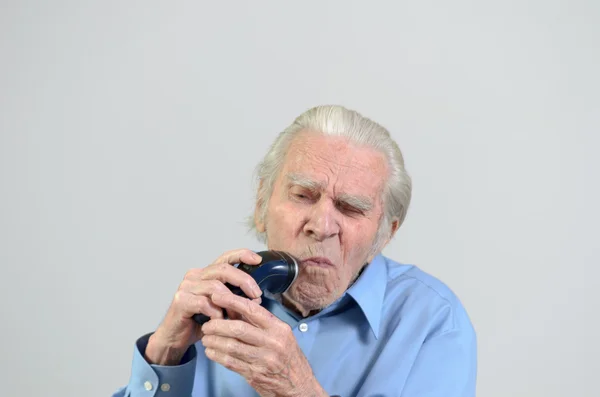 Elderly man shaving with a cordless electric razor — Stock Photo, Image