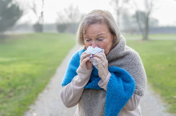 Senior woman blowing her nose on a tissue — Stock Photo, Image