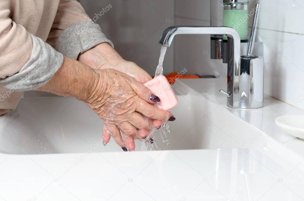 Elderly woman washing hands under tap