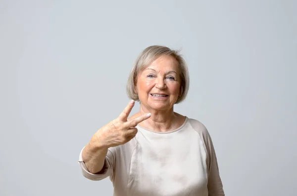 Старшая женщина показывает V признаки — стоковое фото