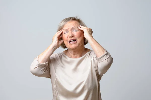 Senior woman with her hands to her temples — Stock Photo, Image