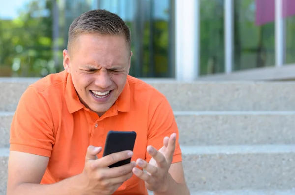 Frustrato giovane uomo gesticolando al suo telefono cellulare — Foto Stock