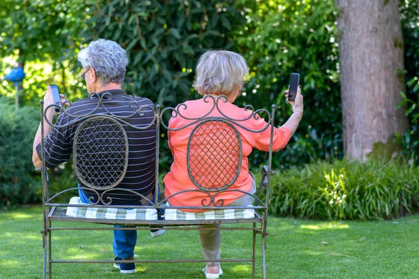 Senior couple sitting on bench with smartphones — Stock Photo, Image