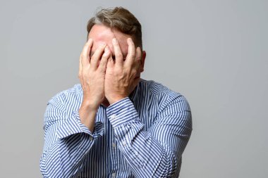 Yüzünü elleriyle kapsayan orta yaşlı adam