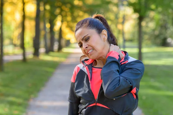 Woman holding her painful neck in park