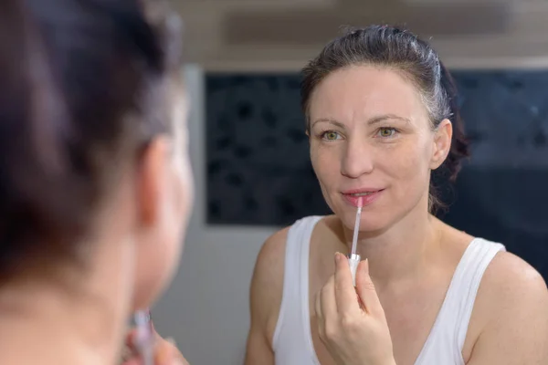 Mujer aplicando un brillo de labios pastel moderno — Foto de Stock