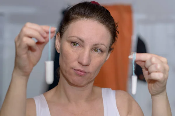 Woman holding up two tampons, one large, one small