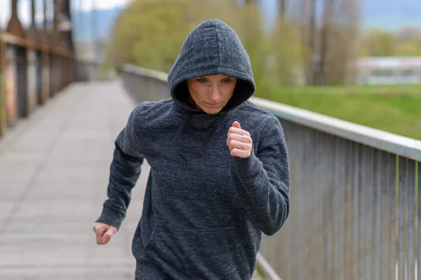 Αθλητική γυναίκα σε μια κουκούλα τρέξιμο πέρα από μια γέφυρα — Φωτογραφία Αρχείου