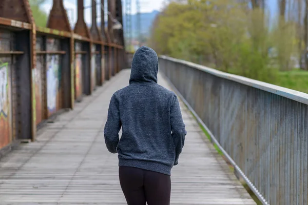 Karcsú nő visel egy kapucnis pulcsit, jogging a híd — Stock Fotó