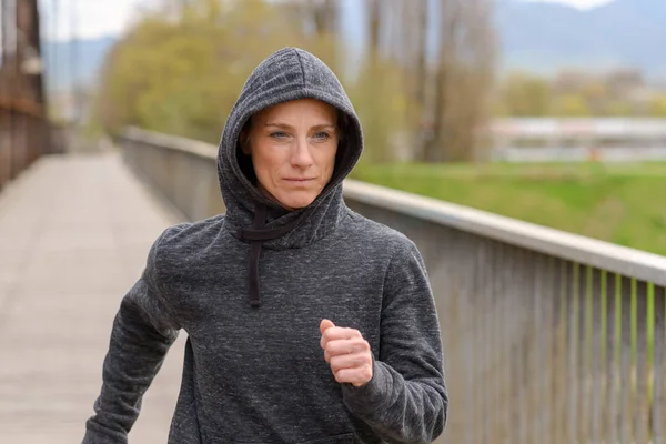 Kvinna i en hoodie jogging över en gammal bro — Stockfoto