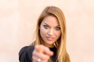 Onun fotoğraf makinesi ile odak, yüzüne karşı tarafsız studio arka plan üzerinde parmakla uzun sarı saçlı çekici gülümseyen samimi kadın