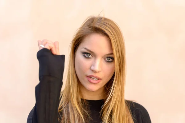 Attractive smiling friendly woman with long blond hair pointing her finger at the camera with focus to her face over a neutral studio background