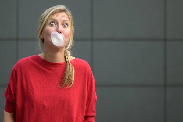 Blond woman blowing a bubble with bubblegum