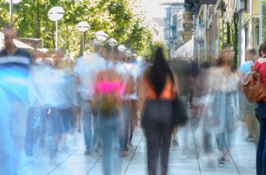 Renkli, bulanık bir kalabalık Parlak, işlek bir şehir kaldırımında yürüyor.