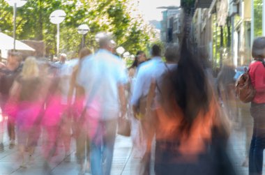 Parlak bir caddede yürüyen renkli, bulanık bir kalabalık..