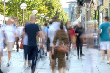 Parlak bir caddede yürüyen renkli, bulanık bir kalabalık..