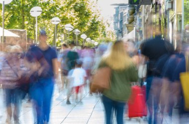 Renkli, bulanık bir kalabalık Parlak, işlek bir şehir kaldırımında yürüyor.