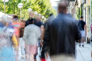 Renkli, bulanık bir kalabalık Parlak bir şehir kaldırımında yürüyor.