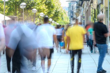 Renkli, bulanık bir kalabalık Parlak bir şehir kaldırımında yürüyor.