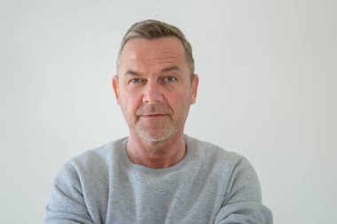 Gri kazaklı yakışıklı ve arkadaş canlısı orta yaşlı bir adamın ön göğüs portresi. Gri bir kazak giymiş, sakin bir yüzle kameraya bakıyor.