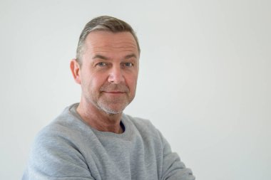 Gri kazaklı orta yaşlı bir adamın yarım dönüşlü portresi. Gülümseyerek kameraya bakıyor.