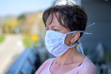 Coronavirus ya da Covid-19 salgını sırasında yüz maskesi takan bir kadın balkonda dikiliyor.