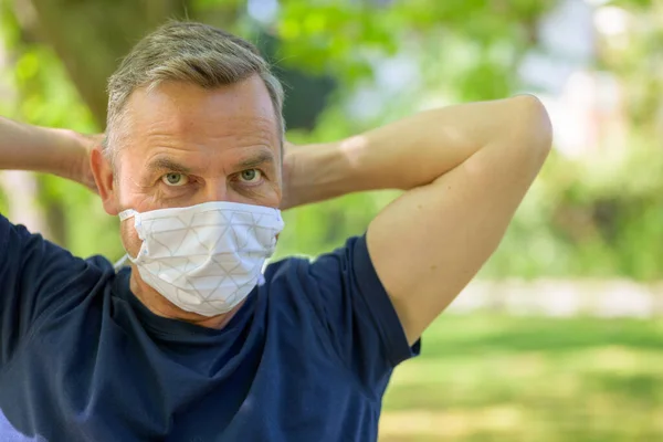 Middle-aged man fitting a surgical mask to his face outdoors in a spring park during the coronavirus or Covid-19 pandemic in a close up portrait