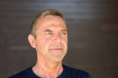 Çekici, düşünceli, traşsız, orta yaşlı bir adam. Düşünceli bir yüz ifadesiyle, fotokopi alanı olan gri bir duvara yakın çekim yapıyor.