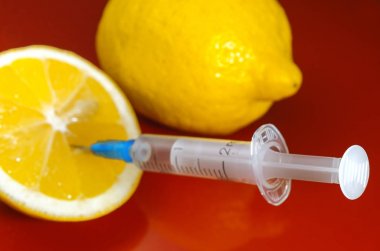 Limon ve şırınga kırmızı bir arka plan üzerinde. Vitamin ilaçları karşı. C vitamini.