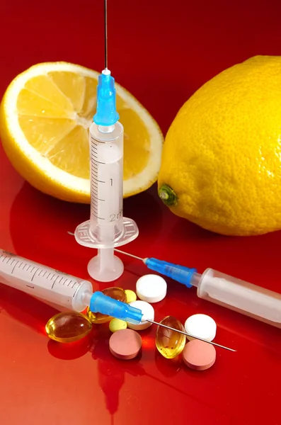 Limones y jeringa sobre fondo rojo. Vitaminas contra medicamentos. Vitamina C . — Foto de Stock