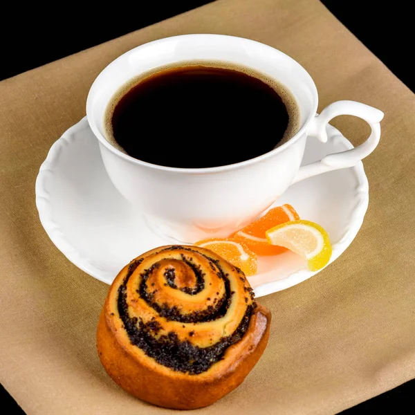 A cup of coffee, a bun with poppy seeds and fruit jelly.