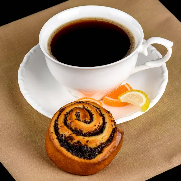 A cup of coffee, a bun with poppy seeds and fruit jelly