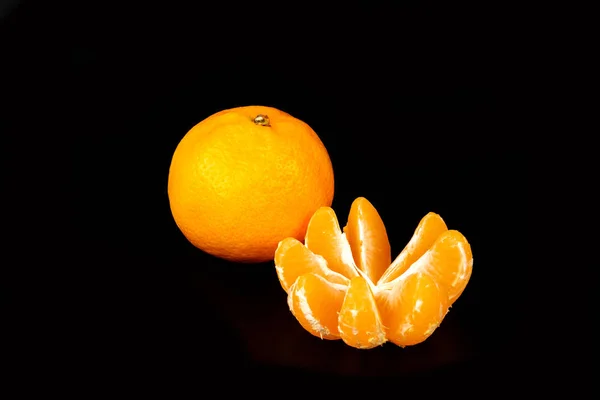 One fresh mandarin and one a peeled on a black — Stock Photo, Image