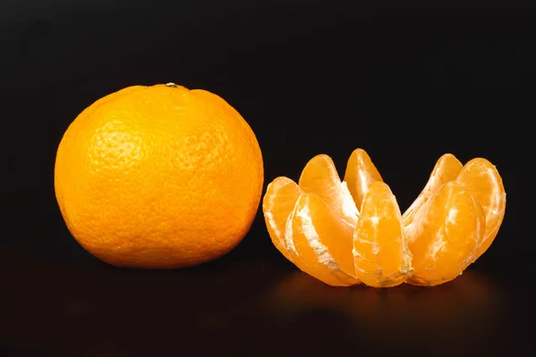 One fresh mandarin and one a peeled on a black — Stock Photo, Image