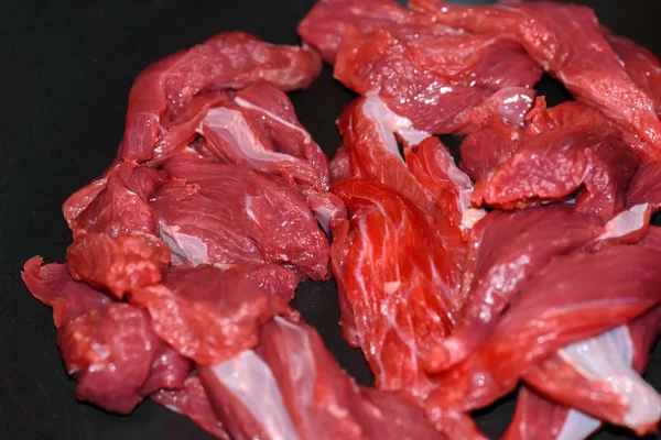 Pedaços de carne fresca jazem no fundo de uma frigideira preta close-up . — Fotografia de Stock