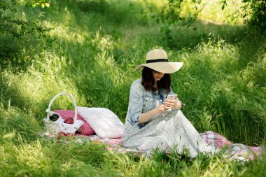 Yaz saati. Genç kadın bir ormanda piknik üzerinde bir sm görünüyor