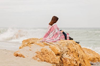 Genç kadın bir halı ile kaplı sahil üzerinde oturur ve okur