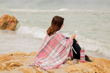 Genç kadın bir halı ile kaplı sahil üzerinde oturur ve okur