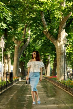 Genç kadın beyaz bir bluz ve mavi bir pe bir parkta yürüyor