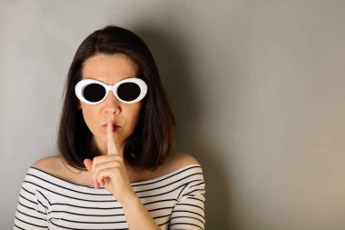 Bir beyaz çizgili üst ve beyaz güneş gözlüklü kadın parmağını tutan