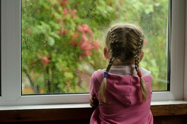 Menina com tranças observando a chuva fora da janela — Fotografia de Stock