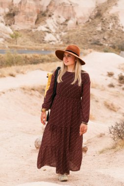 Kahverengi şapkalı ve uzun elbiseli gezgin bir kadın çöl vadisinde ve kayalarda yürüyor. Seyahat ve seyahat tutkusu konsepti. Kapadokya, Türkiye.
