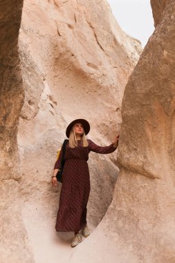 Kum vadisi kayalarında yürüyen kahverengi şapkalı ve uzun elbiseli gezgin bir kadın. Seyahat ve seyahat tutkusu konsepti.