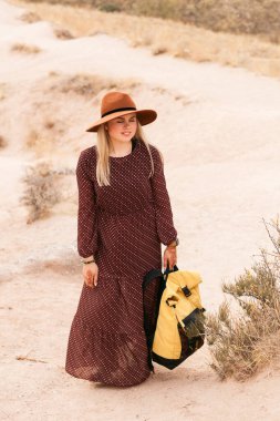 Kahverengi şapkalı ve uzun elbiseli gezgin bir kadın çöl vadisinde ve kayalarda yürüyor. Seyahat ve seyahat tutkusu konsepti. Kapadokya, Türkiye.