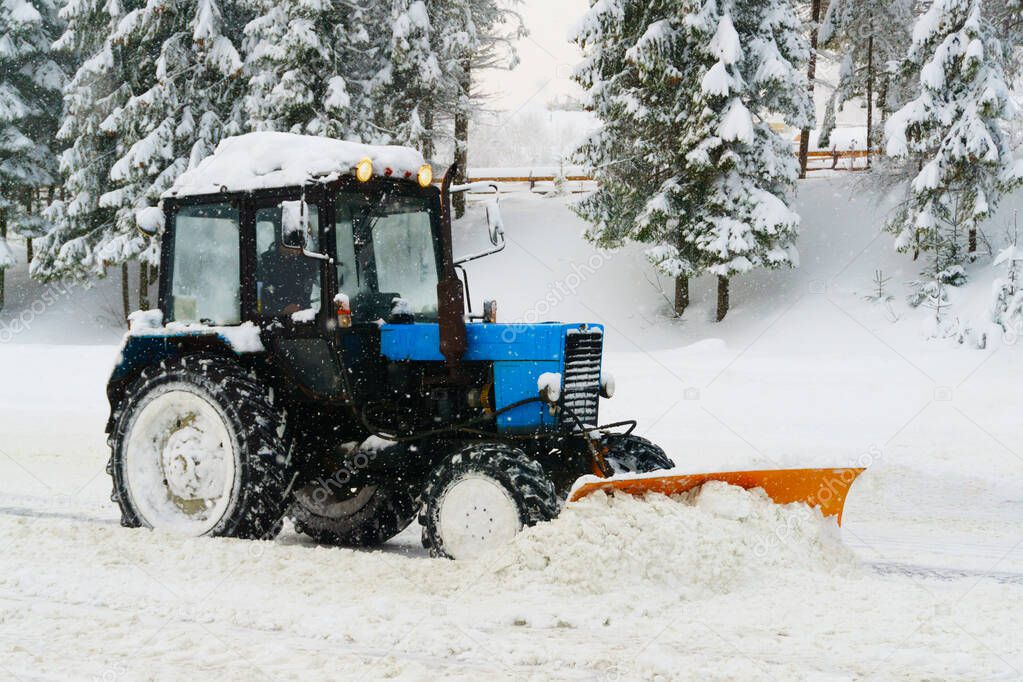 Blue snowblower grader clears snow covered ski resort road in mountains or city street. Winter snowflake snowfall cold fog, mist weather. Horizontal, copy space.