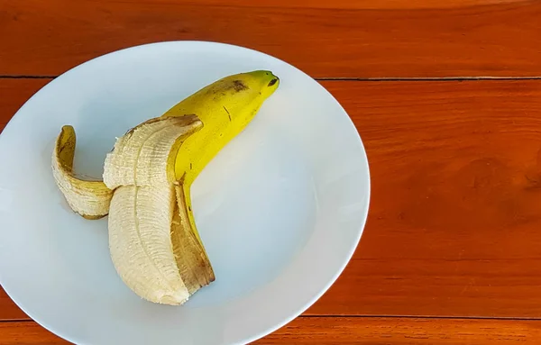 Plátano maduro sobre plato blanco yacía en el suelo de madera . — Foto de Stock