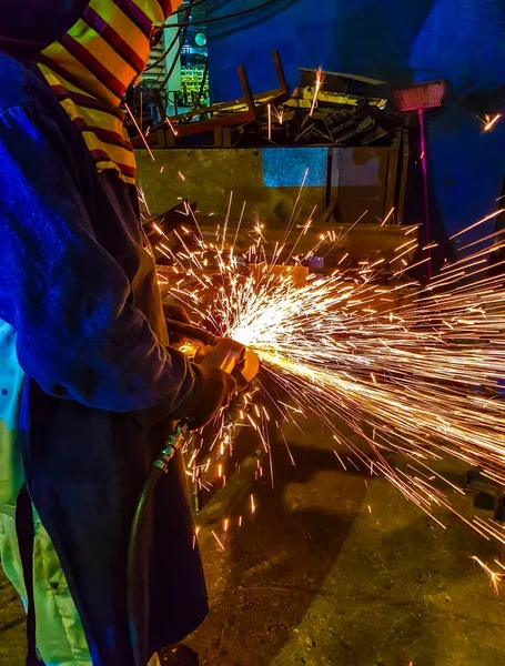 worker grinding metal in manufacturing plant automotive part.